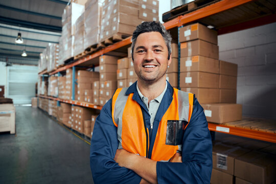 Smiling portrait of a male supervisor standing in warehouse with his arm crossed looking at camera
