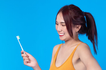 Beauty portrait young asian woman holding toothbrush and smiling on blue background. Concept good oral and dental health.