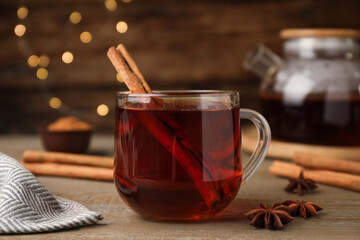 Glass cup of hot tea with aromatic cinnamon on wooden table against blurred lights
