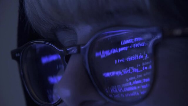 Close up of Programmer hacker working on computer. Code is reflected on his eye glasses. Guy committing cyber crime. Data thief, internet fraud, darknet and cyber security