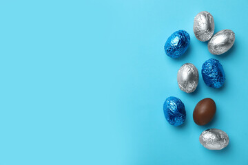 Chocolate eggs wrapped in colorful foil on light blue background, flat lay. Space for text