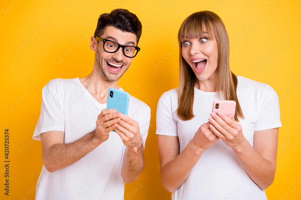 Sticker Photo of shocked funky two persons dressed white t-shirt glasses showing modern devices open mouth isolated yellow color background