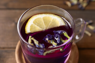 Glass mug of organic blue Anchan with lemon on table, closeup. Herbal tea