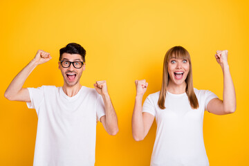 Photo of sweet lucky young couple wear white t-shirt spectacles rising fists isolated yellow color background