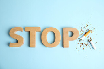 Broken cigarette near word Stop made with wooden letters on light blue background, flat lay....