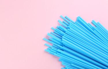 Heap of blue plastic drinking straws on pink background, flat lay. Space for text
