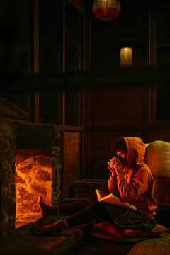 Girl sitting near the fireplace in a cozy home and drinking warm cacao