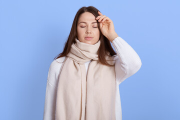 Portrait of unhealthy woman wrapped in warm white scarf, touching her head, suffering headache,...