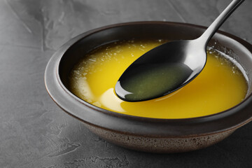 Spoon of clarified butter over bowl on black table, closeup