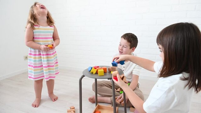 teenager boy 11 years old and his sister 8 years old and girl 4 years old children build a tower from bright wooden cubes play constructor, smile, sit on the floor on a white background