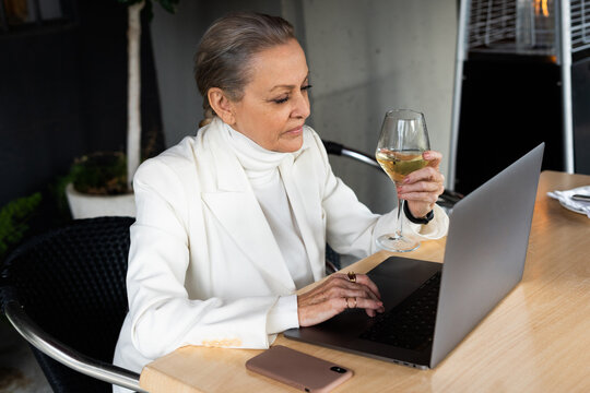 senior business woman checking laptop and drinking a cup of wine at restaurant