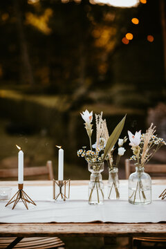 beautiful rustic styled table with linen, vases with dried flowers and candles lit in messing candle holders