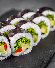 appetizing vegan sushi roll futomaki with pepper cucumber and avocado salad on a black stone plate
