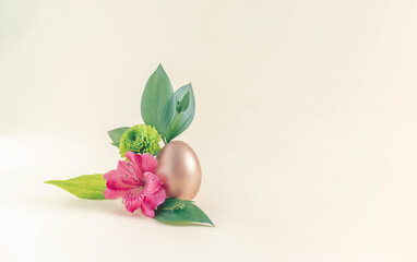 Minimal spring arrangement made of gold Easter egg with pink flower and green leaves on beige background. Creative nature concept with copy space.