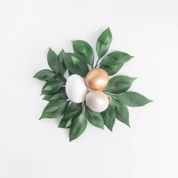 Minimal composition with natural Eater eggs and green tropical leaves on white background. Gold and champagne aestethic. 2021 Easter still life layout.
