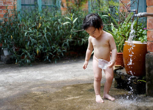 Cute Asian little boy playing and taking shower in front of faucet outdoors