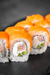 appetizing sushi roll philadelphia with shrimp cheese cucumber and salmon on a black stone plate