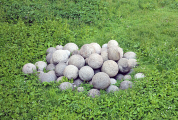 pile of ancient medieval round stone granite cannonballs lie in the green grass
