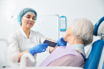 Obraz premium Female stomatologist holding out tooth implant to old woman face