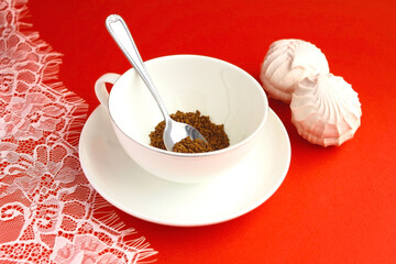 One white cup of coffee, teaspoon, marshmallows and lace tablecloth on a red table.