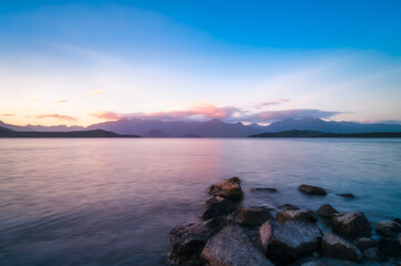 Colorful sunset on the shore at Lake Te Anau with rocks in the water and the mountain range silhouetted in the background in Fiordland National Park, New Zealand, South Island.