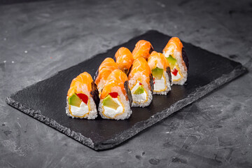 appetizing sushi roll philadelphia with avocado cheese omelette and salmon on a black stone plate