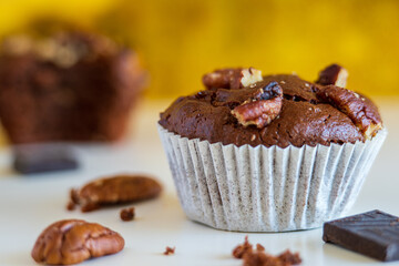 Healthy chocolate muffin, homemade freshly baked and gluten free with pecans, cocoa powder and dark chocolate. Yellow sparkly background with eaten muffin behind. nutrition concept. Side view