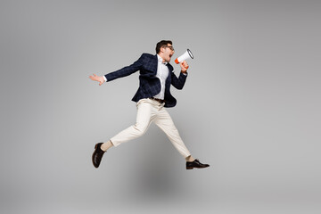 full length of businessman jumping and screaming in megaphone on grey