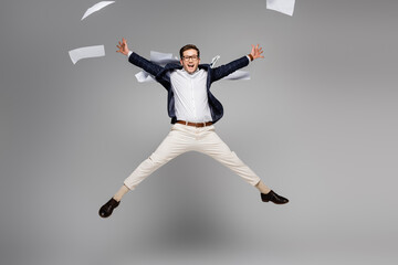 Fototapeta na wymiar full length of cheerful businessman jumping near papers in air on grey