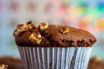 Healthy gluten free chocolate muffin. Homemade, freshly baked good, with pecans, cocoa powder and dark chocolate. Party, colorful sparkly background. Nutrition concept. Close up with side view 