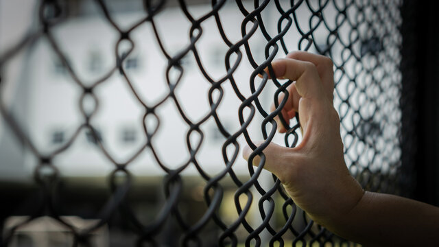 Slavery trade and trafficking victim concept of woman prisoner in jail being tortured, punished or abused in violation with hand holding cage wire mesh