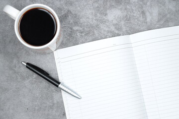 coffee, blank notebook and a pen on cement concrete surface floor.