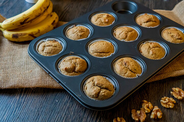 Healthy, gluten free, banana oats muffins ready to eat. Nutritional snack hot from the oven, placed in a muffin tray. Dark table and rustic cloth with selective focus. Side view
