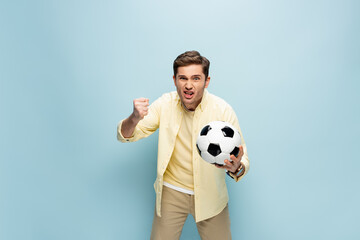 irritated man in yellow shirt holding football on blue