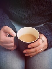Coffee mug in women's hands with a knitted sweater. Woman holds hot coffee. Black coffee, evening coffee. Vintage. Lifestyle.