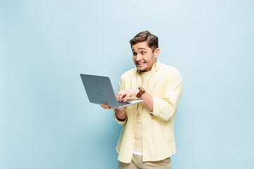 happy young man in shirt typing on laptop isolated on blue