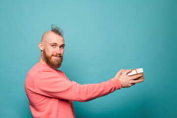 Bearded european man in casual peach isolated on turquoise background excited holds out gift box to left