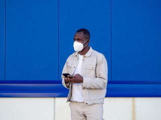 Hombre afroamericano usando su móvil mientras viste una mascarilla para protegerse del coronavirus...