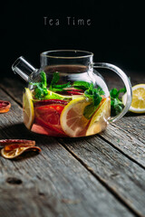 Tea with citrus and mint in a glass teapot on a dark background