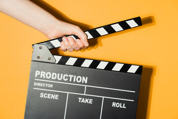 Obraz premium Hand holding film clapperboard on yellow studio background