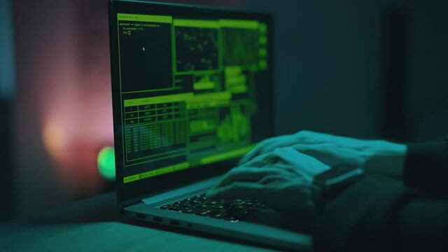 Hacker is working on laptop at night. Hands are typing a virus code at keyboard or hacking website. Closeup. Concept of bitcoin cryptocurrency and wallet hack. Software coder or blockchain developer