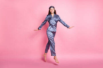 Full length body size photo of brunette wearing sleepwear jumping smiling isolated on pastel pink...