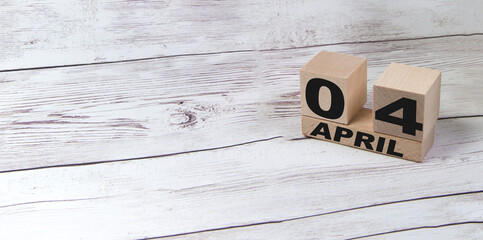 Cube-shaped calendar for April 04 on a wooden surface with a blank space for text on a light wooden table-copy the text space next to the April symbol