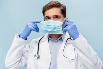 young doctor in white coat with stethoscope wearing medical mask isolated on blue