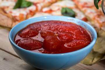ciotola con passata di pomodoro dentro , sullo sfondo una pizza margherita