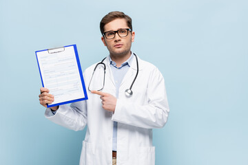 doctor in glasses and white coat pointing with finger at clipboard with medical card lettering on blue