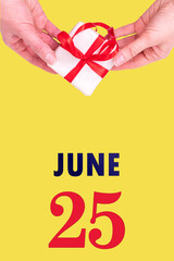 June 25th. Festive Vertical Calendar With Hands Holding White Gift Box With Red Ribbon And Calendar Date 25 June On Illuminating Yellow Background.Summer month, day of the year concept.