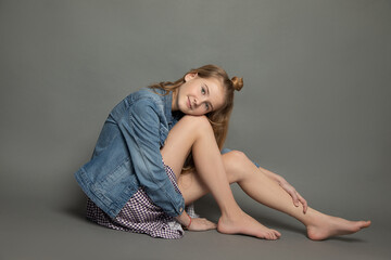 very young charming barefooted woman teenager girl sitting in studio on gray background, head on...