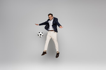 Fototapeta na wymiar full length of smiling businessman playing football while levitating on grey