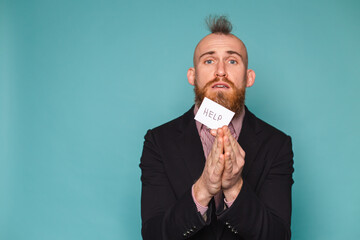 Bearded european businessman in dark suit isolated on turquoise background holding paper with help sign sad unhappy begs